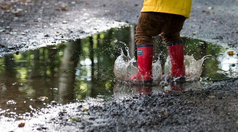 child with red rain boots jumping in a puddle
