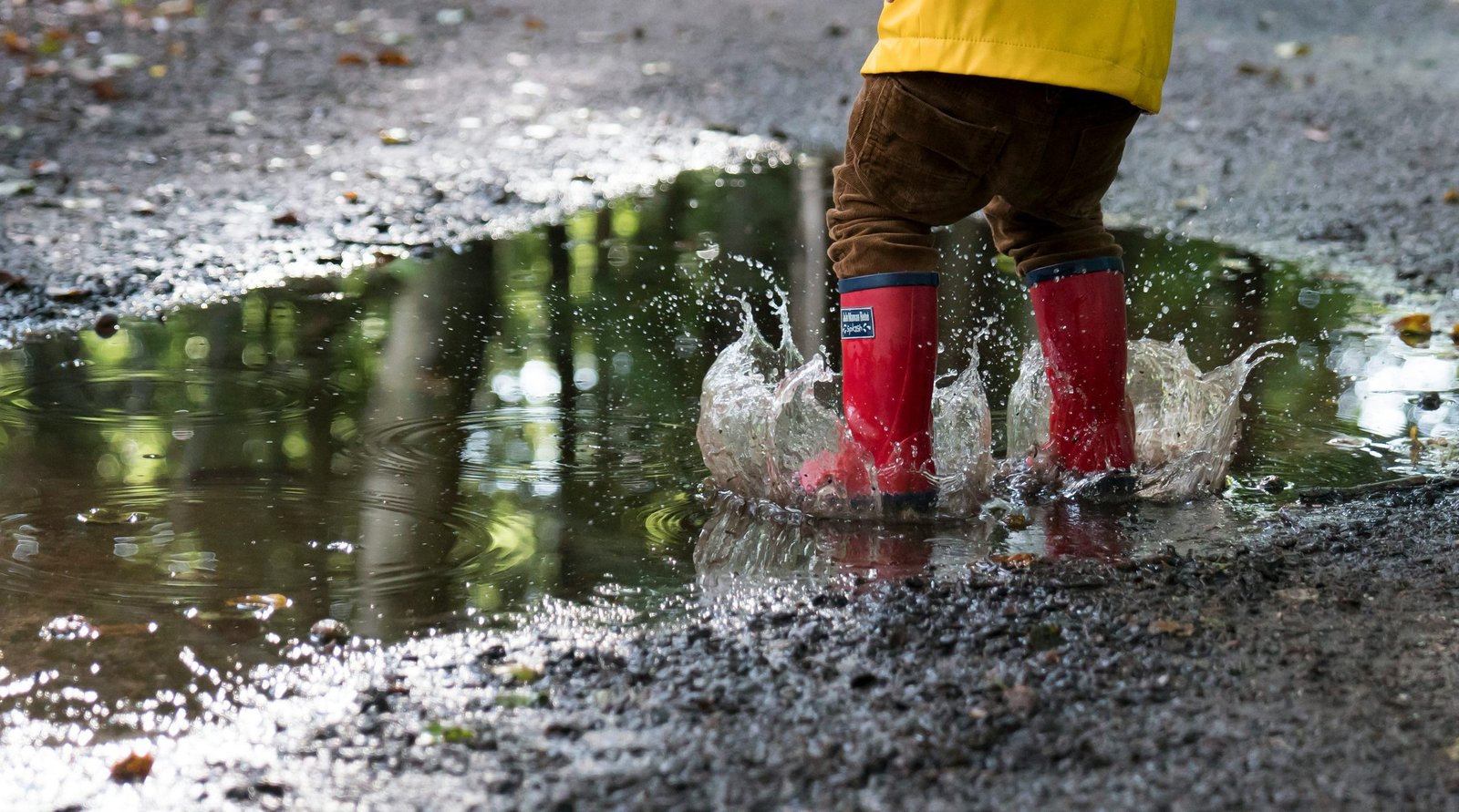 child with red rain boots jumping in a puddle